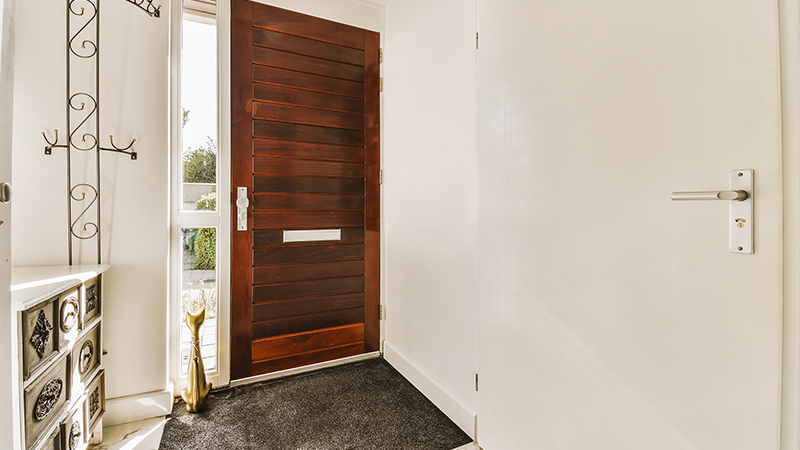 a hallway with a door in the middle and black carpet on the floor next to the front door is a mirror