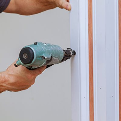 Carpenter using a brad nail gun to complete framing trim Air gun for nailing Carpenter using a brad nail gun to complete framing trim Air gun for nailing using nail gun